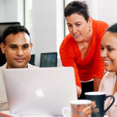 Two university students looking at laptop while lecturer looks over their shoulder. Image, UQ